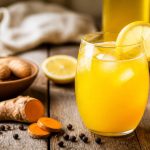Limonade détoxifiante au curcuma et poivre noir servie dans un grand verre avec des rondelles de citron bio et des glaçons, fond en bois clair