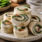 Wraps apéritifs aux épinards, ricotta et tomates séchées coupés en rondelles, présentés sur une ardoise avec des piques apéritifs